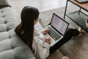 A woman works from home on her laptop while sitting on the floor with poor posture.