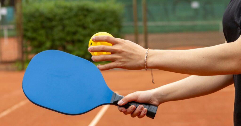 Two hands holding a pickleball paddle and pickleball. 