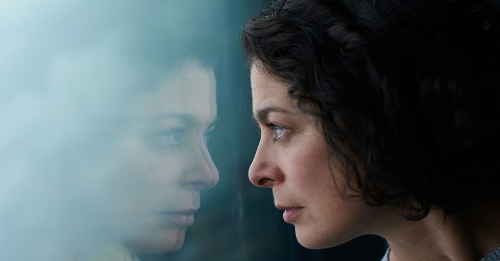 A person looking at their reflection in a window.